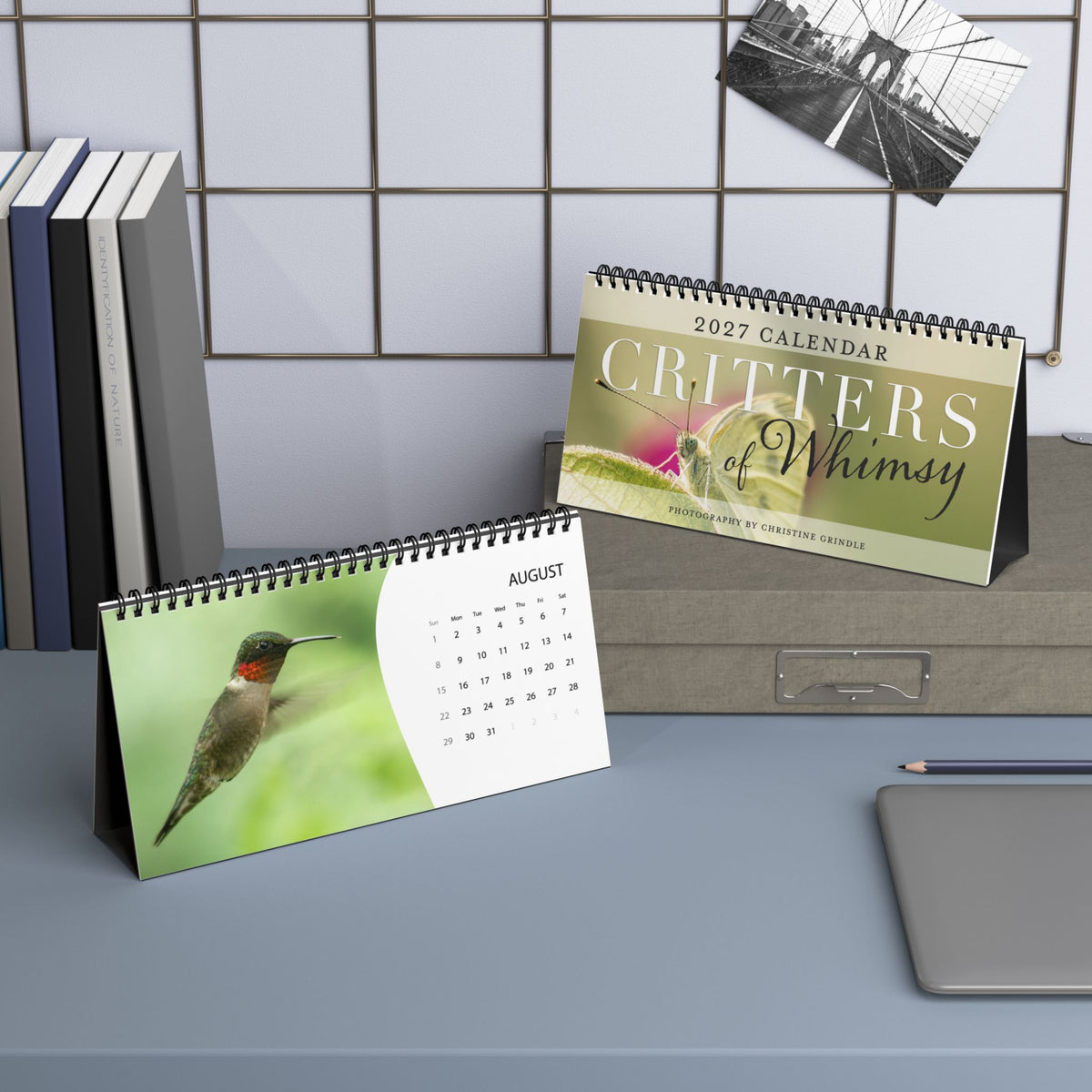 Terra Conserva Critters of Whimsy 2027 desk calendars displaying the butterfly cover and August hummingbird page in a workspace