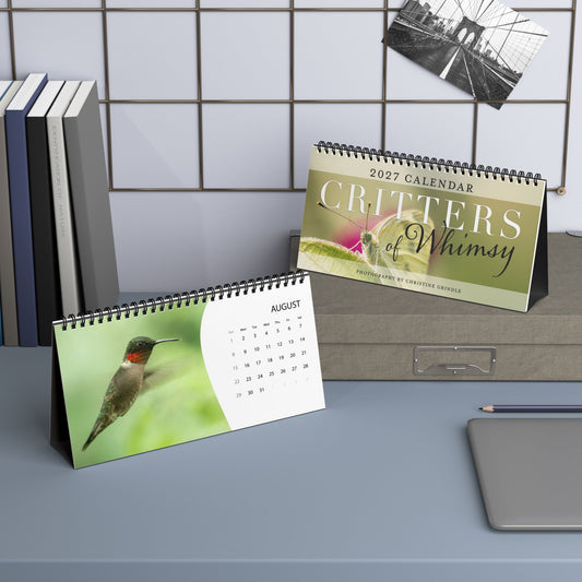Terra Conserva Critters of Whimsy 2027 desk calendars displaying the butterfly cover and August hummingbird page in a workspace